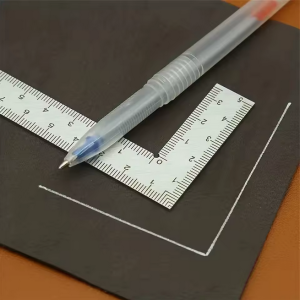 Precision square ruler and white gel pen used to draw accurate right-angle lines on black material.