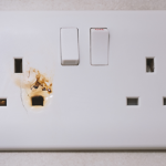 Standard UK double outlet socket with visible burn marks and signs of electrical arcing