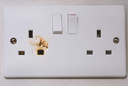 Standard UK double outlet socket with visible burn marks and signs of electrical arcing